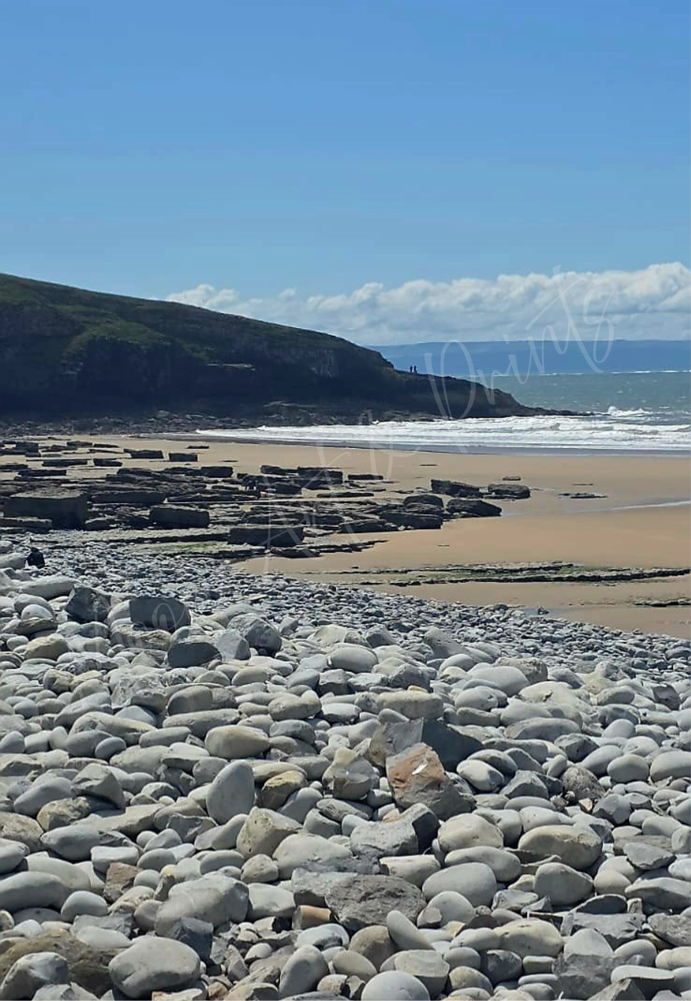 Rocky British coastline with smooth pebbles, sandy shore, and ocean waves beneath blue sky